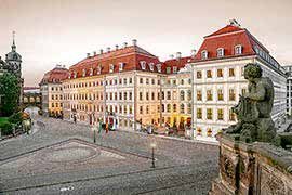 Exterior of the Taschenbergpalais: the long Baroque façade with red roofs above the cobbled square, a sandstone statue in the right foreground