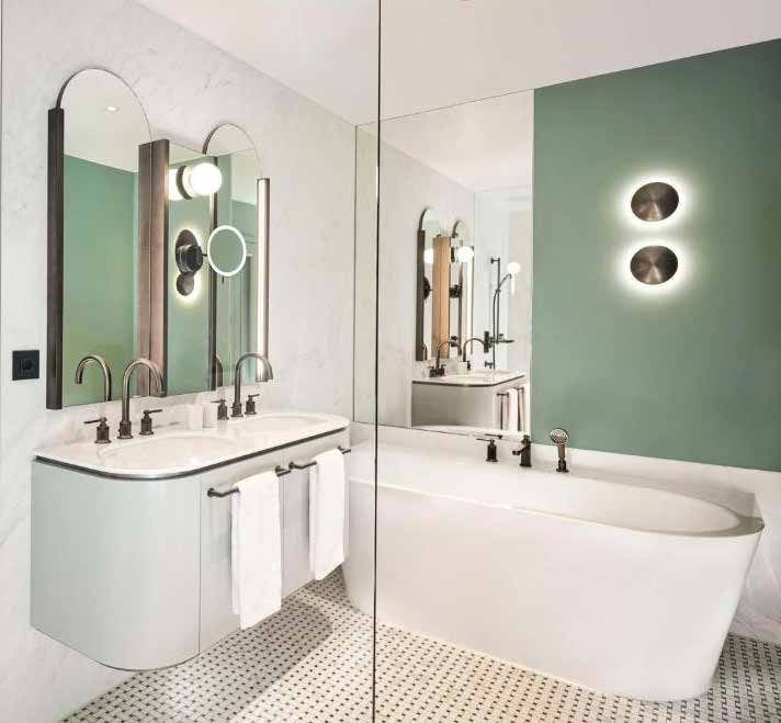Bathroom of a guest room: a white double vanity with round-arched mirrors, a bathtub behind a glass wall and a mint-green wall with two round wall lights