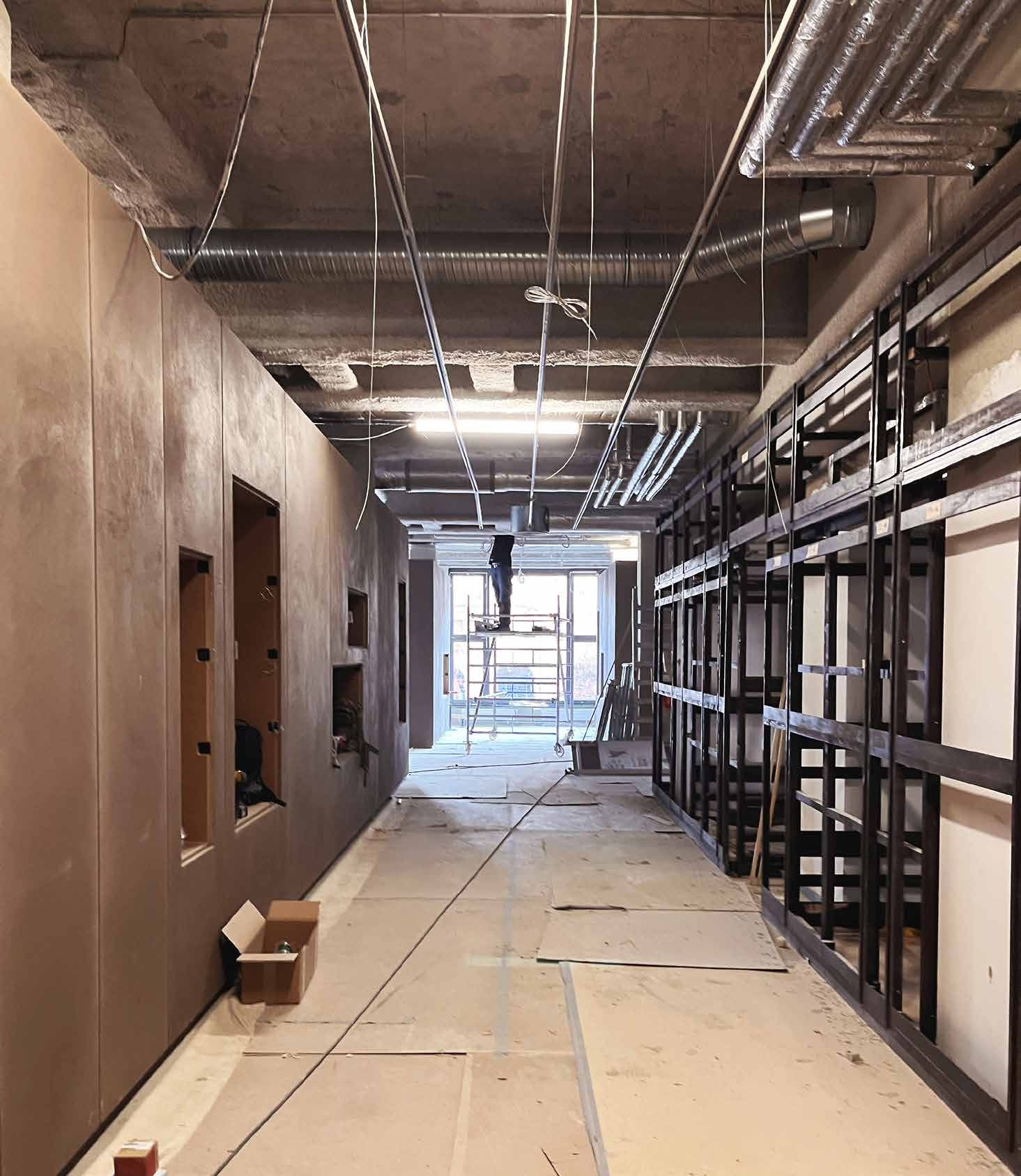 Cantiere Papenbreer: un lungo corridoio con pareti in cartongesso, soffitto a vista e scaffalature in acciaio nero