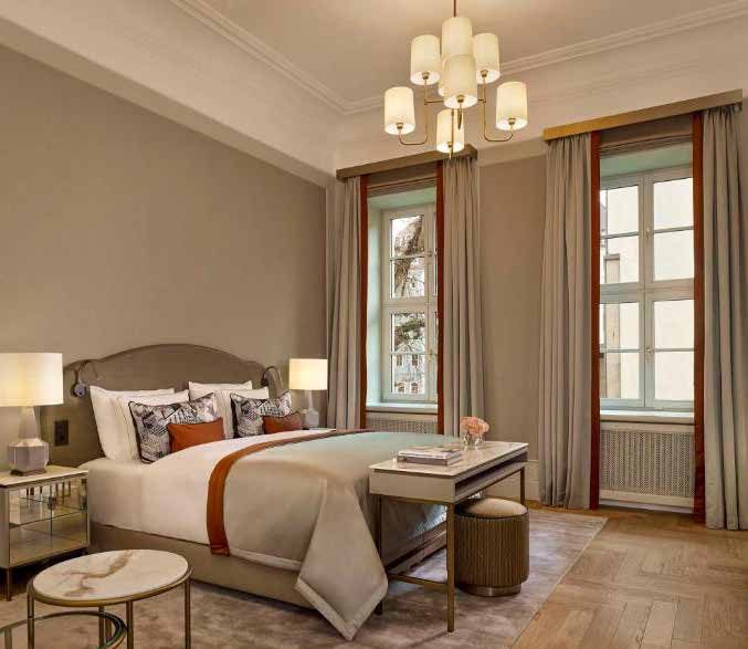 Room in design type I: an upholstered bed with a pale bedspread and a rust-red stripe, a brass chandelier, tall curtained windows and herringbone parquet