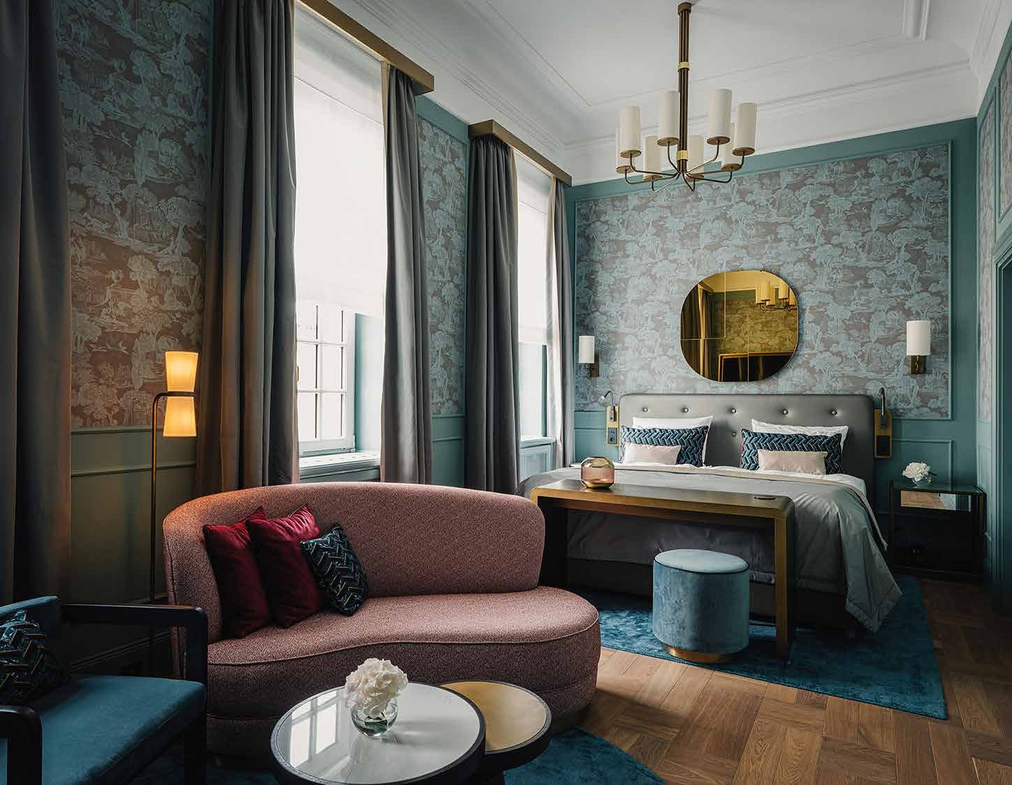 Room in design type II: turquoise-green walls with mural wallpaper, a pink sofa, a round brass mirror above the bed and a blue carpet