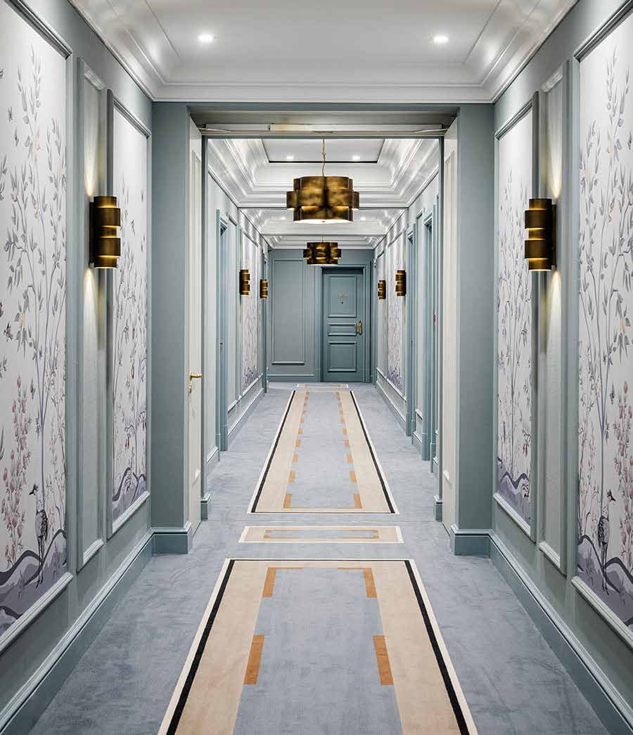 Hotel corridor after the refurbishment: blue-grey wall panels with floral mural wallpaper, brass wall lights and a carpet with a pale linear pattern
