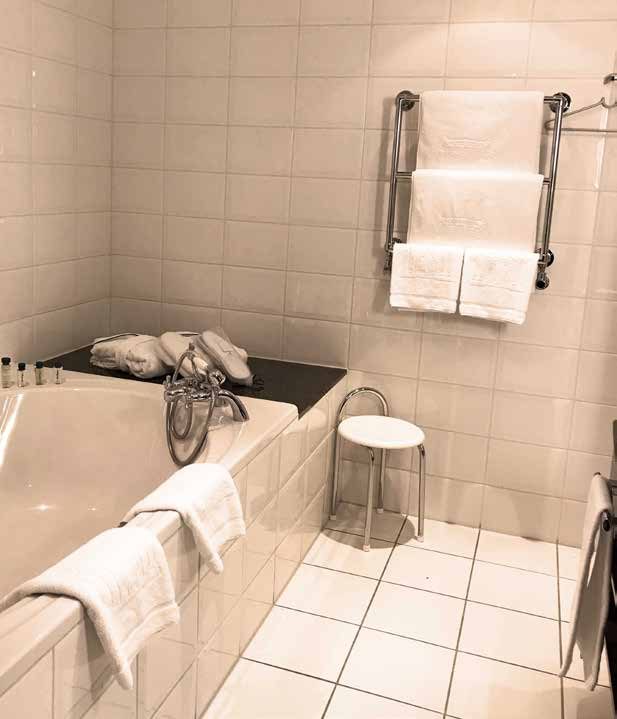 The bathroom of the bridal suite before the refurbishment: white-tiled walls, a built-in bathtub and a heated towel rail