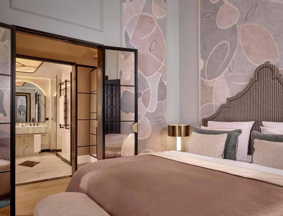 The bridal suite today: a bed with a tall headboard against pink mural wallpaper, with a view through black-framed glass doors into the bathroom