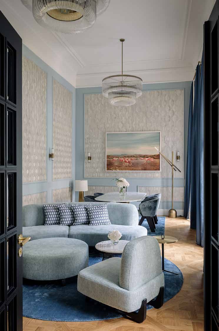 The living room of the bridal suite today: wall panels framed in light blue, a glass chandelier and rounded upholstered furniture on a blue carpet