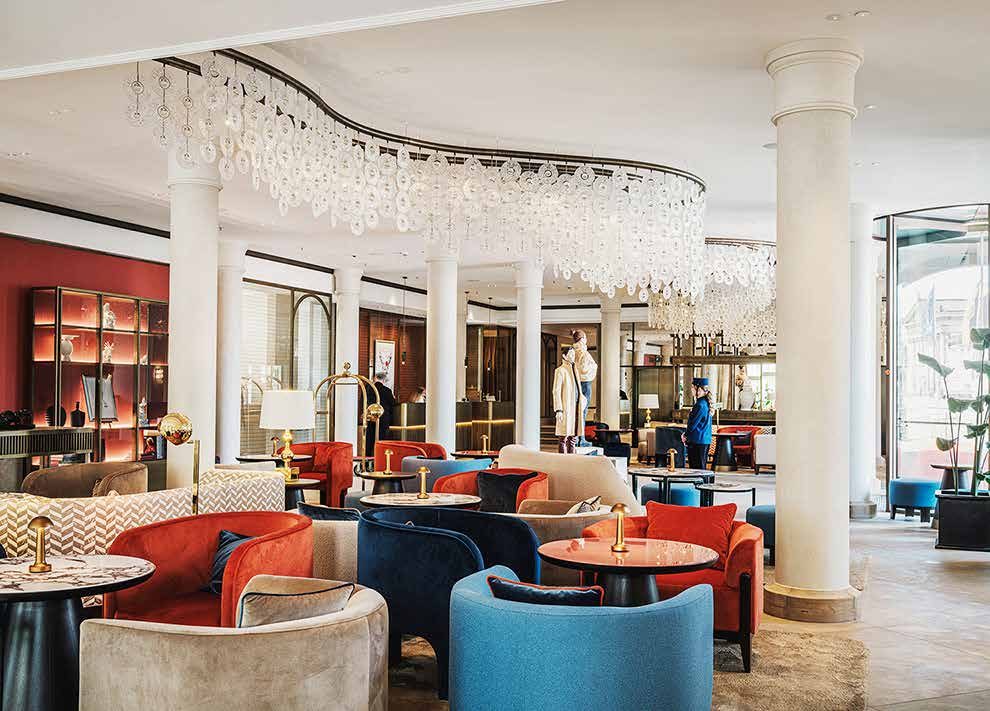 The lobby today: a sweeping glass chandelier above seating groups with red, blue and beige armchairs between white columns