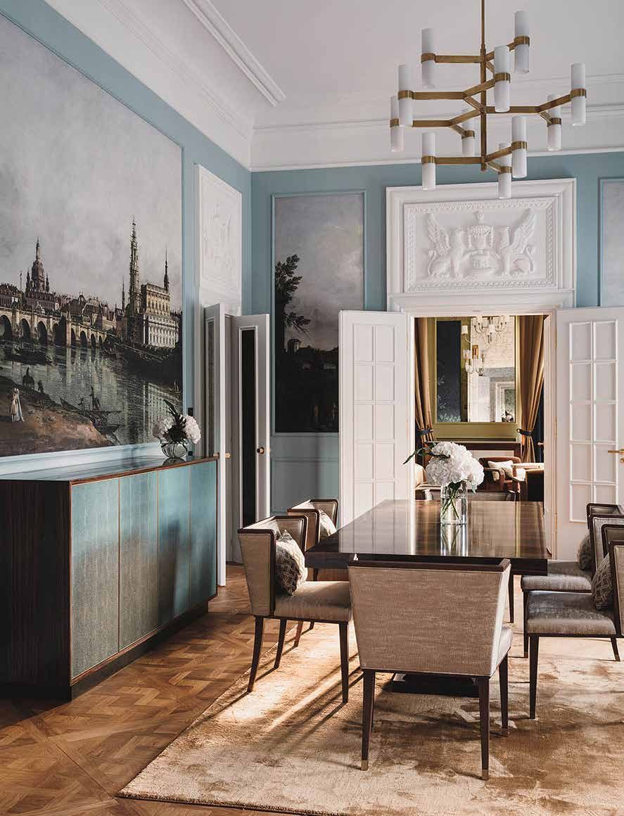 The King’s living room today: light blue walls with a historic view of Dresden as a mural, a stucco relief above the door, a dining table with chairs and a brass chandelier