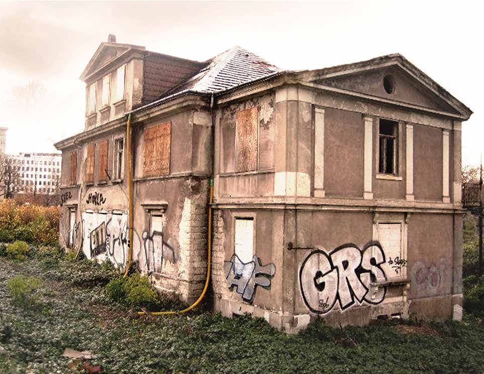 Vorher: dieselbe Eckansicht als Ruine — vernagelte Fenster, abgeplatzter Putz, Graffiti und Wildwuchs vor dem Sockel